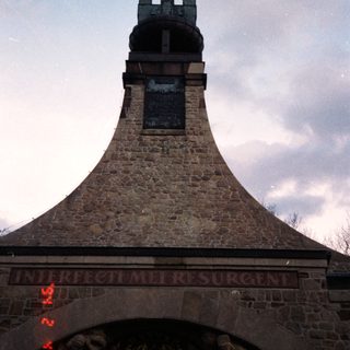 Stone bell tower with cross and Latin inscription.