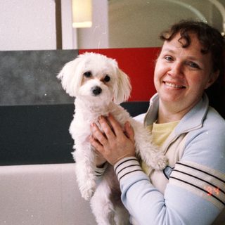 Woman smiling while holding small white dog indoors.