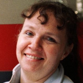 Woman smiling while holding small white dog indoors.