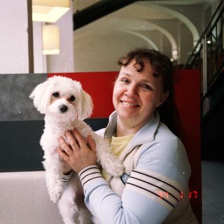 Woman smiling while holding small white dog indoors.