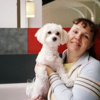 A woman holding a small white dog indoors.