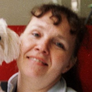 A woman holding a small white dog indoors.