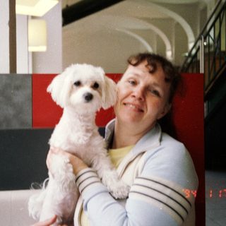 A woman holding a small white dog indoors.