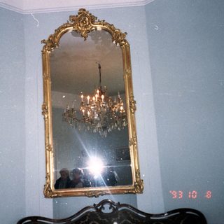 Elegant gold-framed mirror with chandelier reflection.