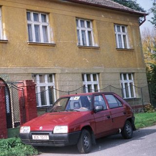 Two-story yellow house with red car parked outside.