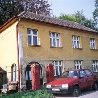 Two-story yellow house with red car parked outside.
