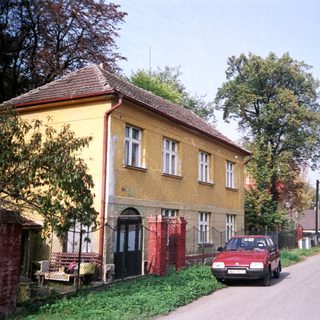 Quaint street with yellow house, parked car, and greenery.