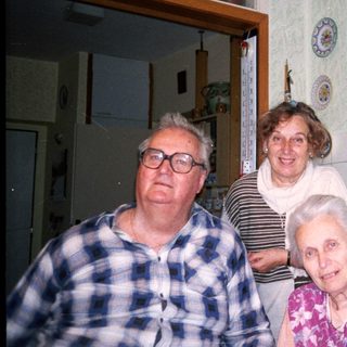 Three elderly people posing together in a vintage kitchen.
