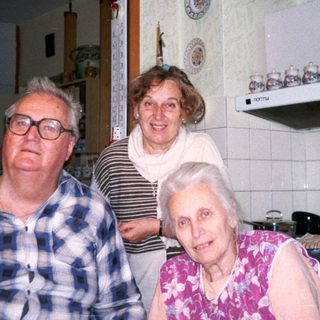 Three elderly people posing together in a vintage kitchen.