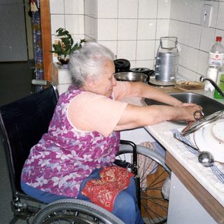 Elderly person in wheelchair cooking at kitchen counter.