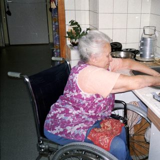 Elderly person in wheelchair cooking at kitchen counter.