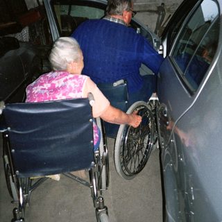 Two elderly people transferring from wheelchair to car.