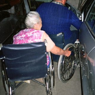 Two elderly people transferring from wheelchair to car.