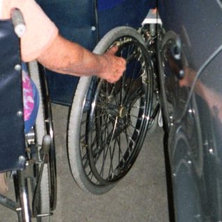 Two elderly people transferring from wheelchair to car.