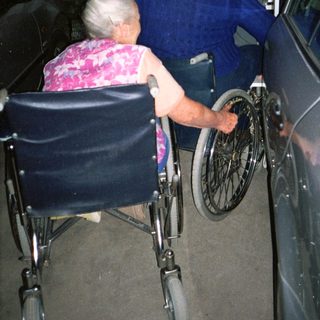 Two elderly people transferring from wheelchair to car.