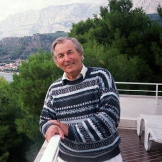 Man posing by waterfront with mountainous background.