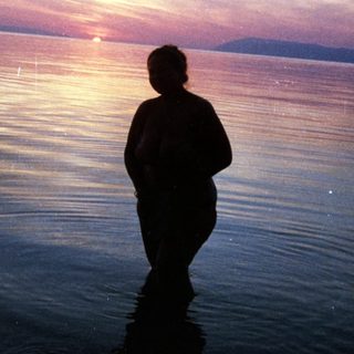 Silhouette standing in shallow water at sunset.