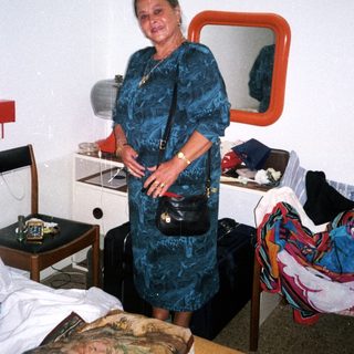 Woman posing in hotel room with luggage and clothes.