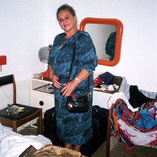 Woman posing in hotel room with luggage and clothes.