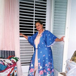 Woman wearing floral blue kimono by open window.