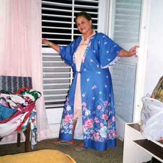 Woman wearing floral blue kimono by open window.