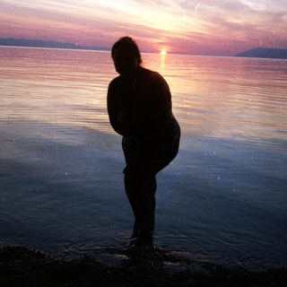 Silhouette of person watching sunset by water.