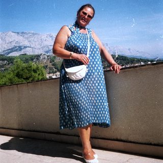 Woman in polka-dot dress posing outdoors near mountains.