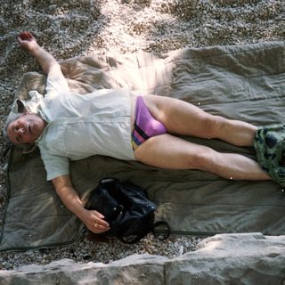 Person relaxing on camping mat near water.