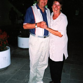 Two elderly people smiling together outdoors at night.
