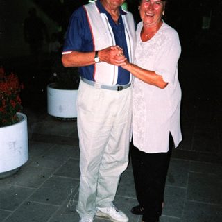 Two elderly people smiling together outdoors at night.