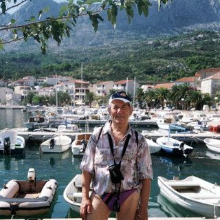 Man posing by marina with boats and coastal town.