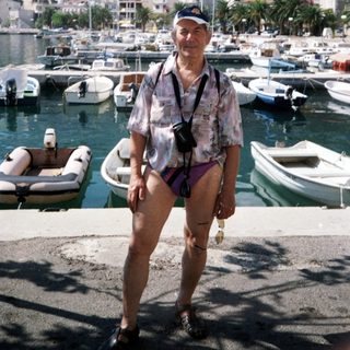 Man posing by marina with boats and coastal town.