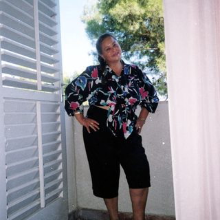 Woman posing confidently in floral blouse and shorts.