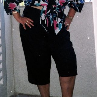 Woman posing confidently in floral blouse and shorts.