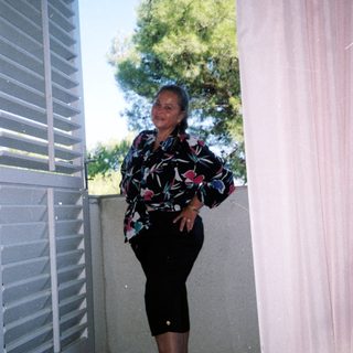 Woman standing in doorway wearing floral top, skirt, and green shoes.