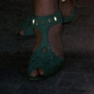 Woman standing in doorway wearing floral top, skirt, and green shoes.