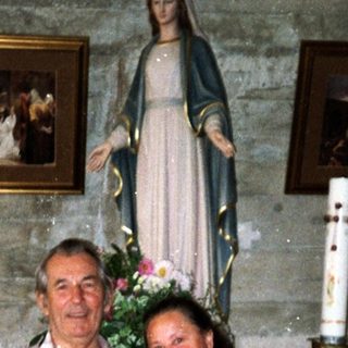 Two people posing indoors near religious statues and artwork.