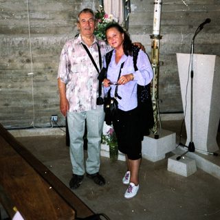Two people posing indoors near religious statues and artwork.