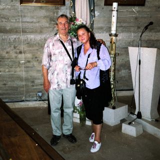 Two people posing indoors near religious statues and artwork.
