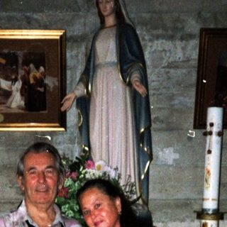 Two people posing indoors near religious statue and altar.