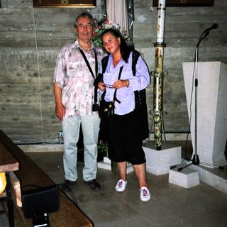 Two people posing indoors near religious statue and altar.
