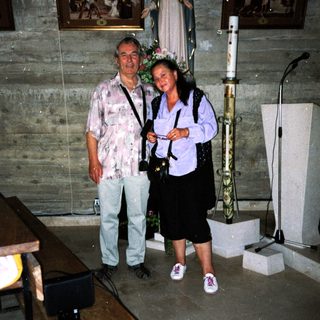Two people posing indoors near religious statue and altar.