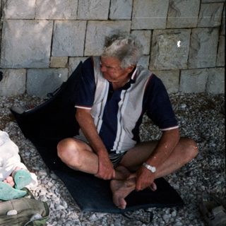 Three people relaxing by a stone wall.