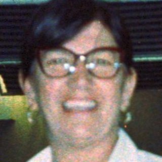 Smiling person in white shirt indoors, possibly restaurant.