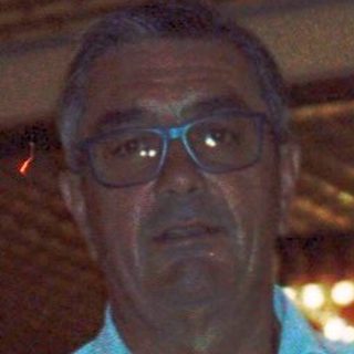 Man in light blue shirt standing indoors near boxes.