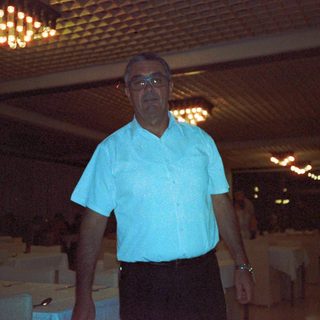 Man in light blue shirt standing indoors near boxes.