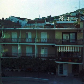 Urban residential buildings with balconies, hilly backdrop.