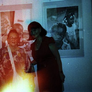 Elderly woman posing with younger woman in gallery.