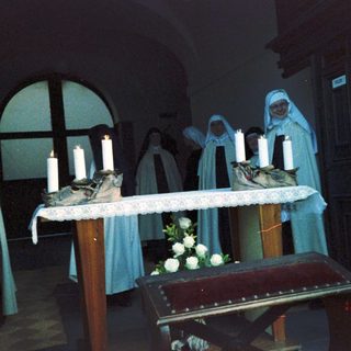 Funeral service with nuns lighting candles at memorial table.