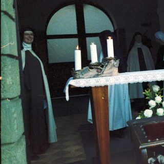 Funeral service with nuns lighting candles at memorial table.